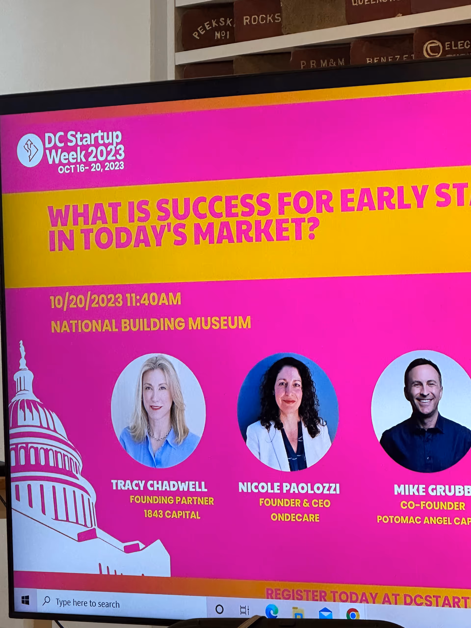 Bright pink and yellow DC Startup Week banner displayed on a monitor inside a building.
