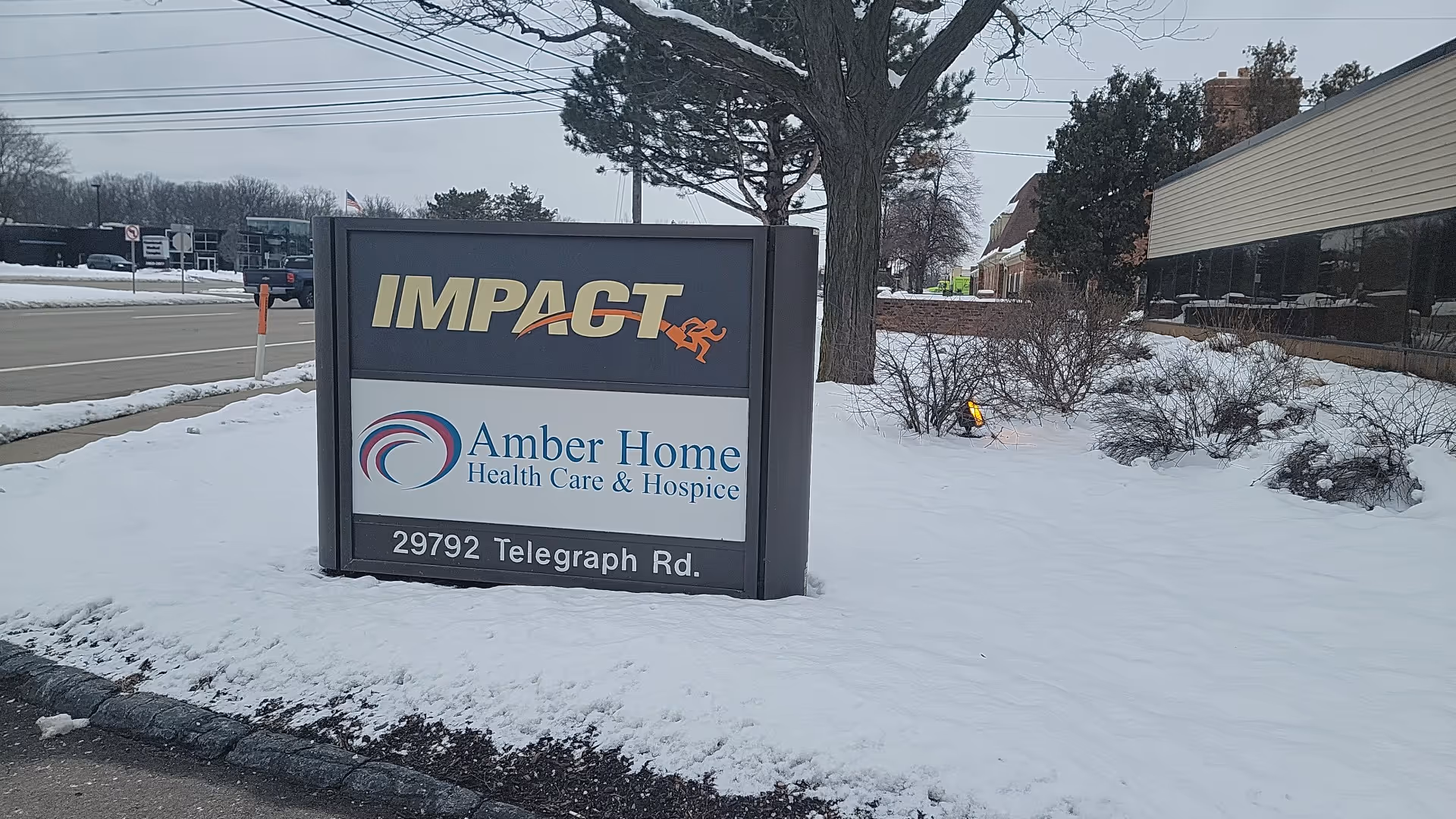 An outdoor sign for Amber Home Health Care & Hospice on a snowy lawn.