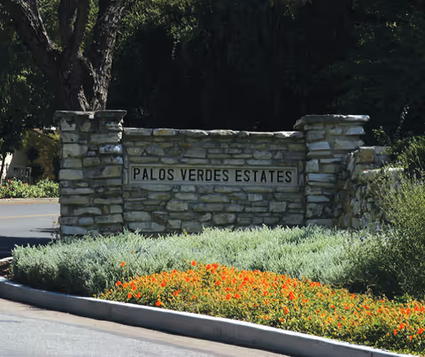 Stone entrance sign reading Palos Verdes Estates with landscaping and a road behind.