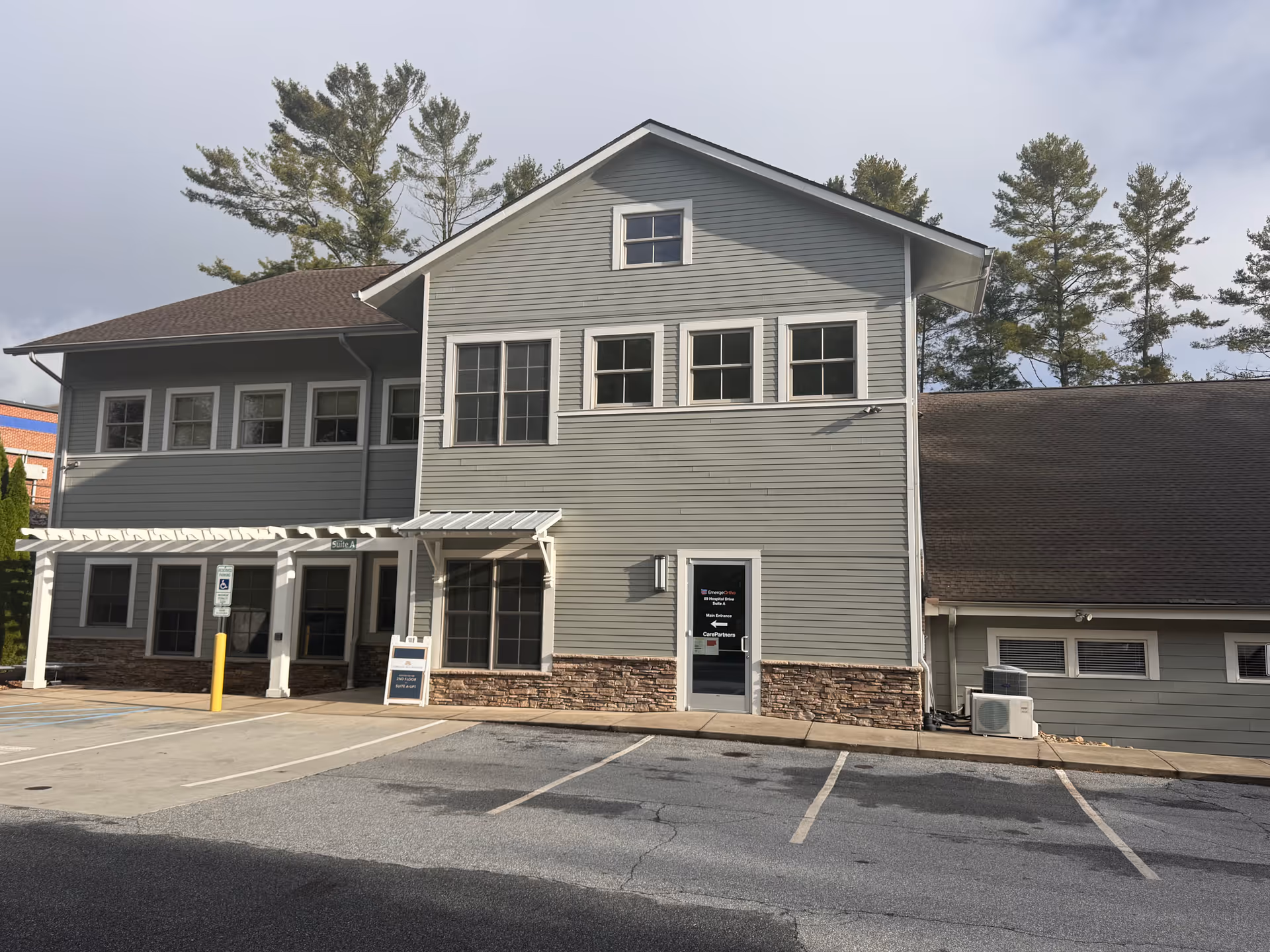 Gray two-story building with stone base and a parking lot in front.