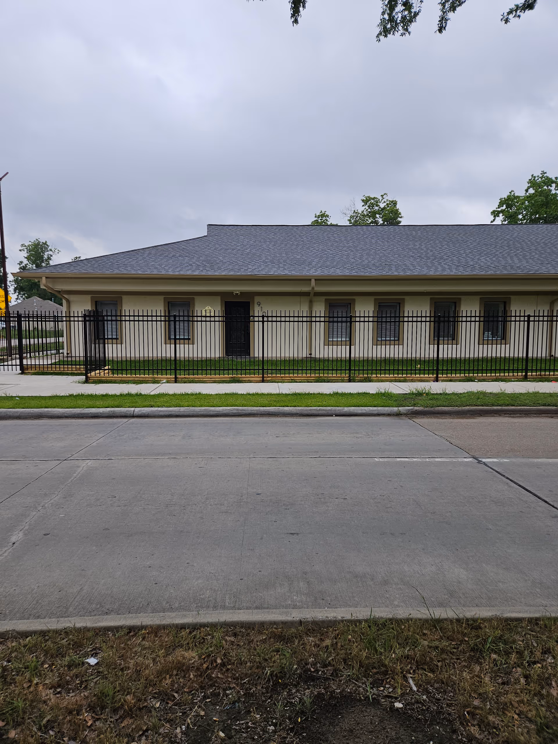 Single-story beige facility behind a black fence along a street.