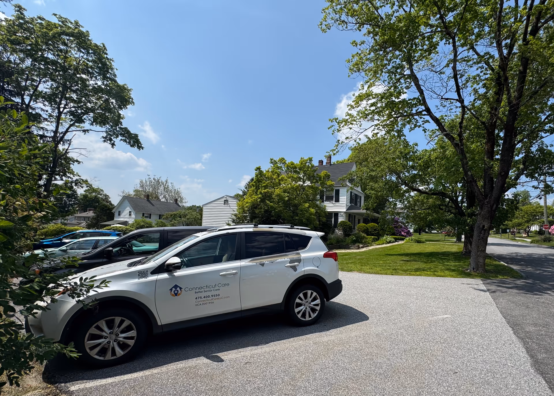 White Connecticut Care vehicle parked in a residential driveway with trees and houses nearby.