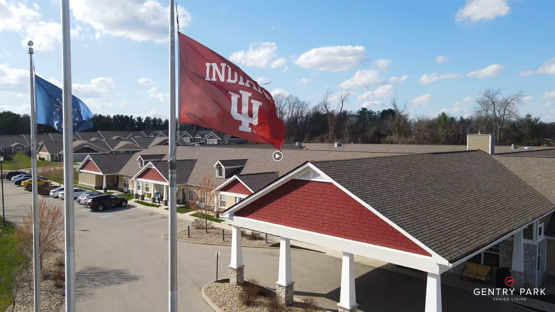 Entrance canopy with flagpoles and a row of single-story residential buildings in a senior living complex.