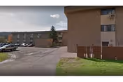Exterior view of a brick senior living facility with parking lot and fence.