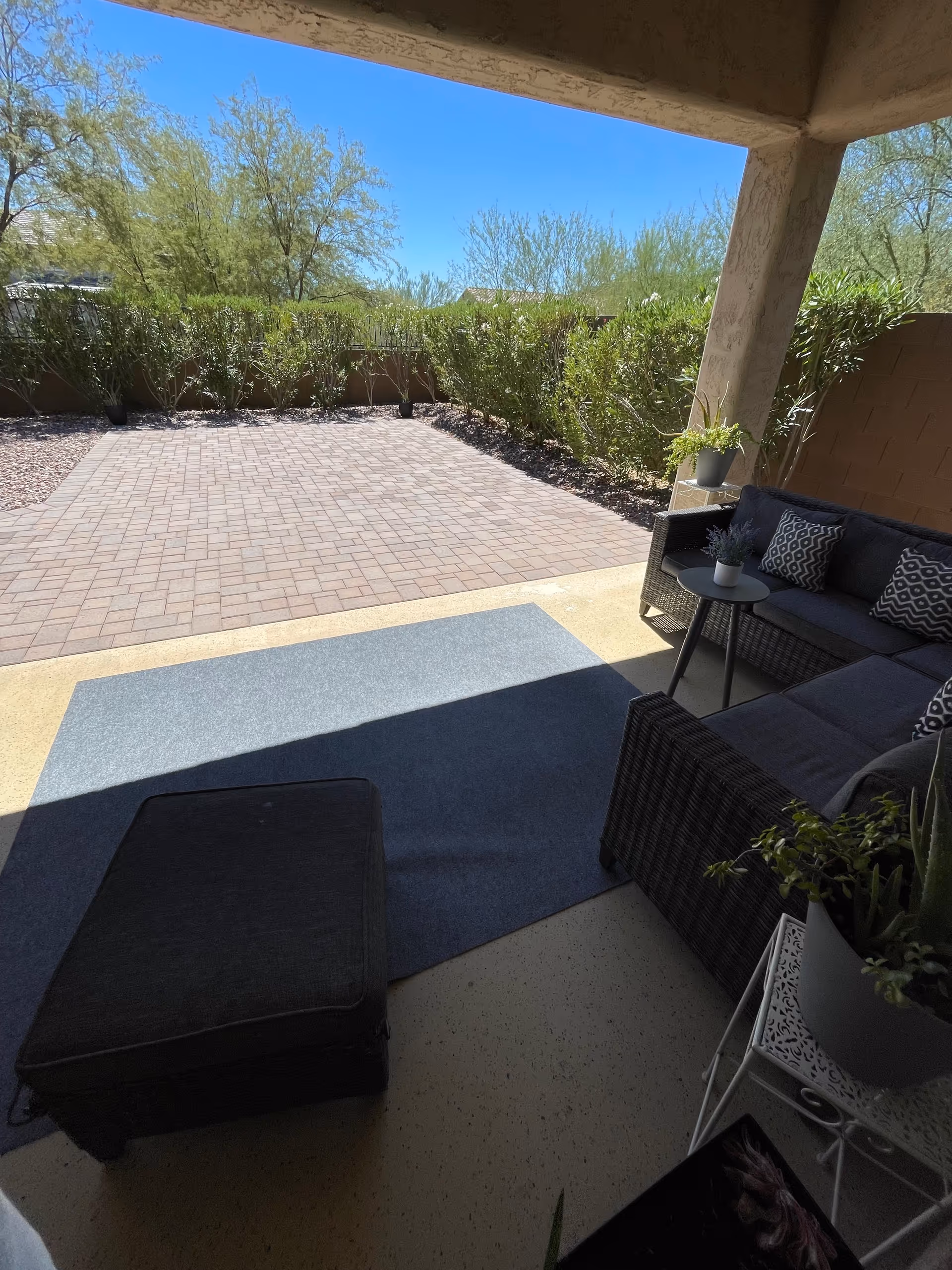 Covered outdoor patio with wicker seating, a blue rug, and potted plants.