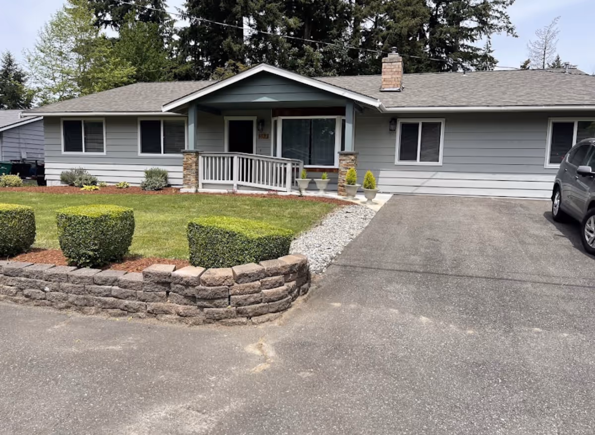 Single-story care home exterior with a front porch, driveway, and neatly pruned shrubs.
