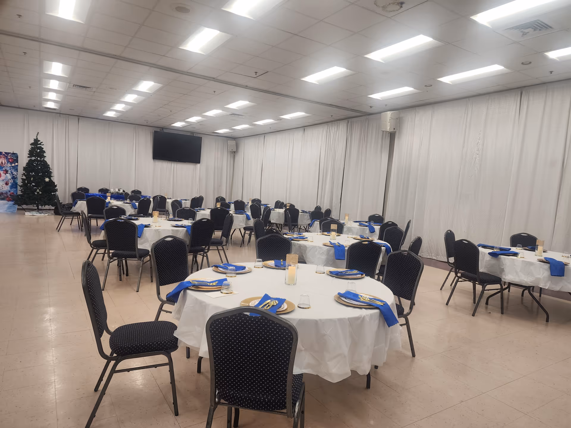 Banquet-style dining hall with round tables, white tablecloths, and blue napkins.