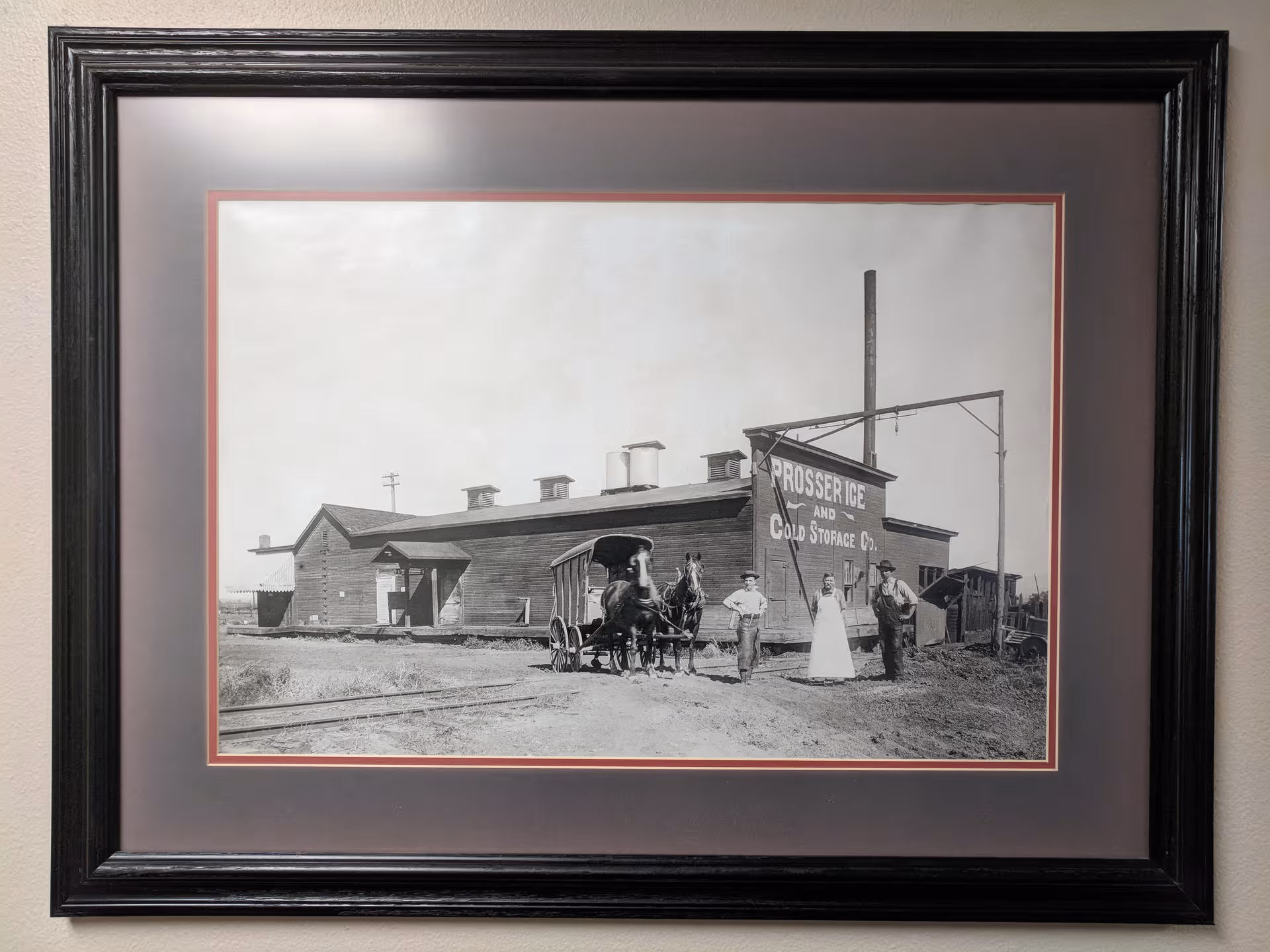 Black-and-white framed photo of a building with a horse-drawn wagon and people.