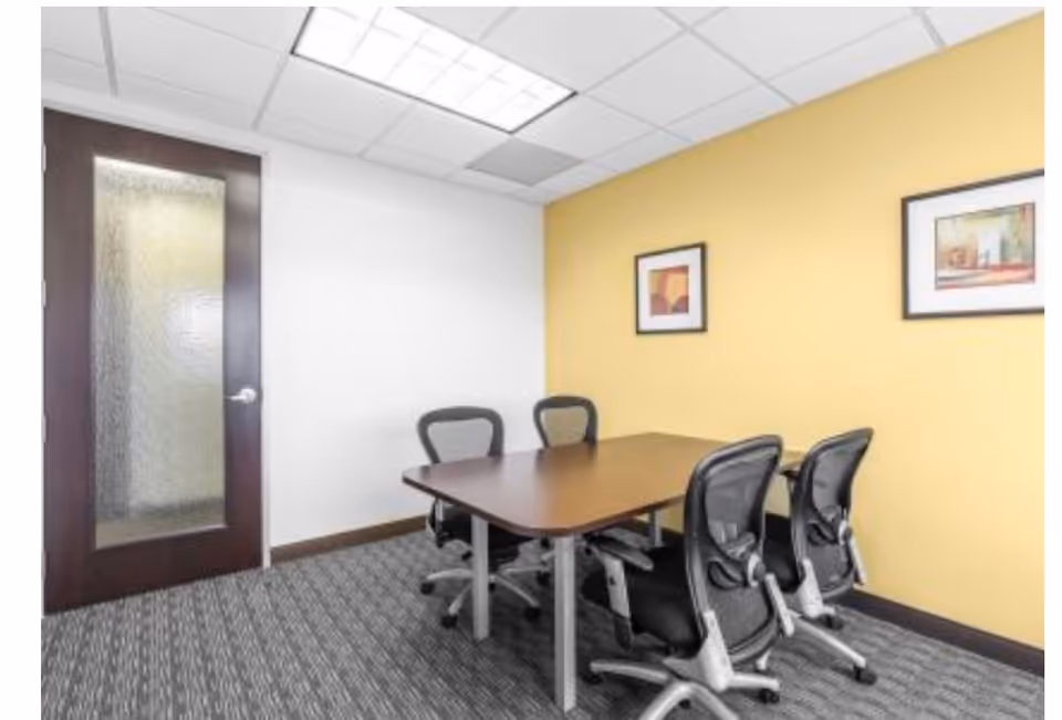 A small conference room with a wooden table and chairs against a yellow wall