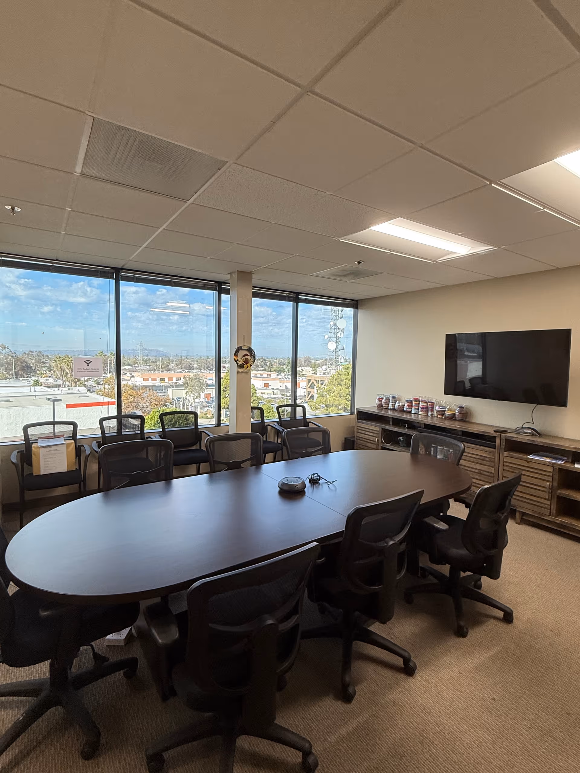 Conference room with a large oval table, multiple chairs, and a wall-mounted TV.