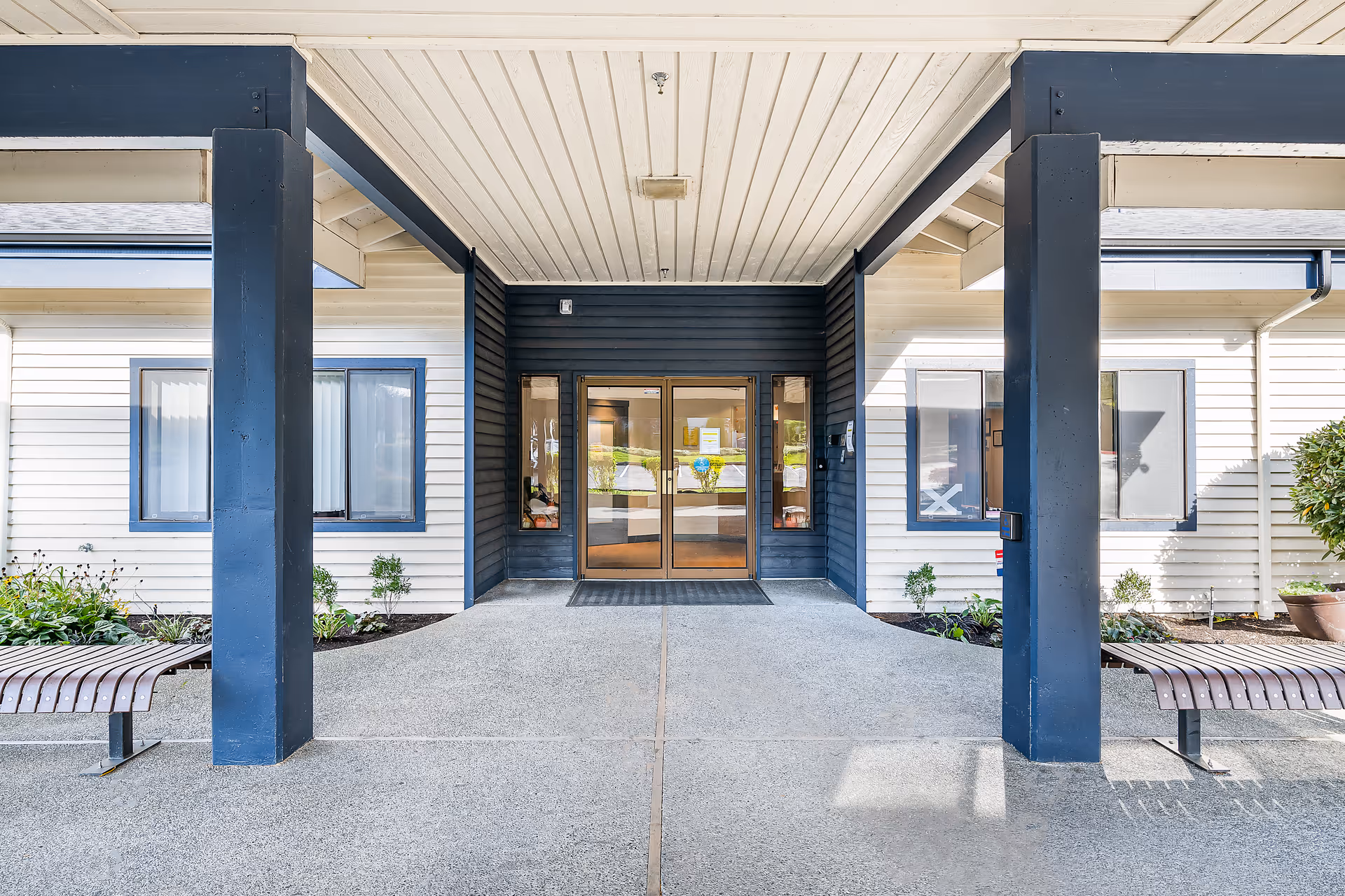 Entrance to a retirement facility with glass doors, blue columns, and benches outside.