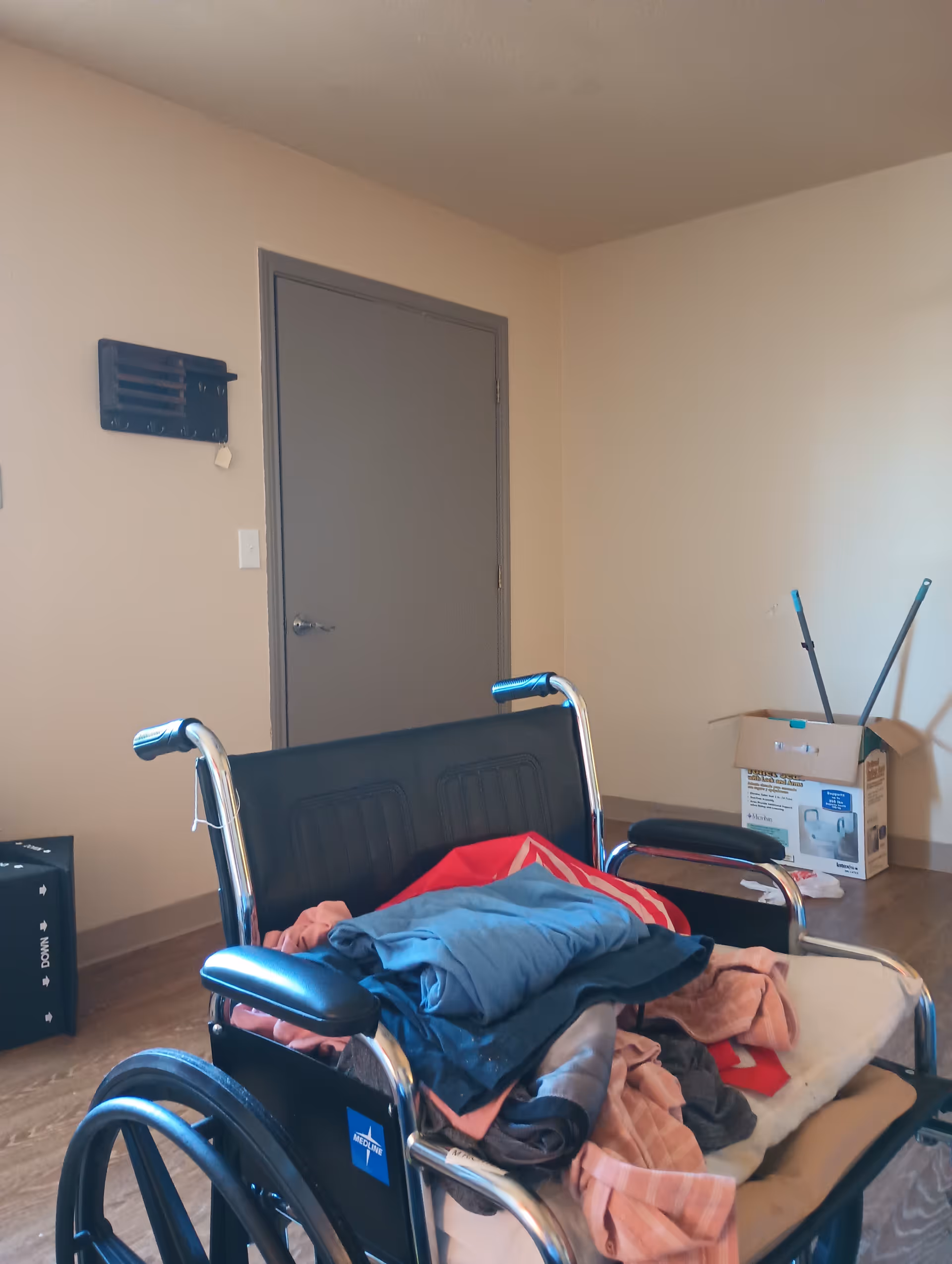 Wheelchair with blankets sits in a bare interior room near a closed door.