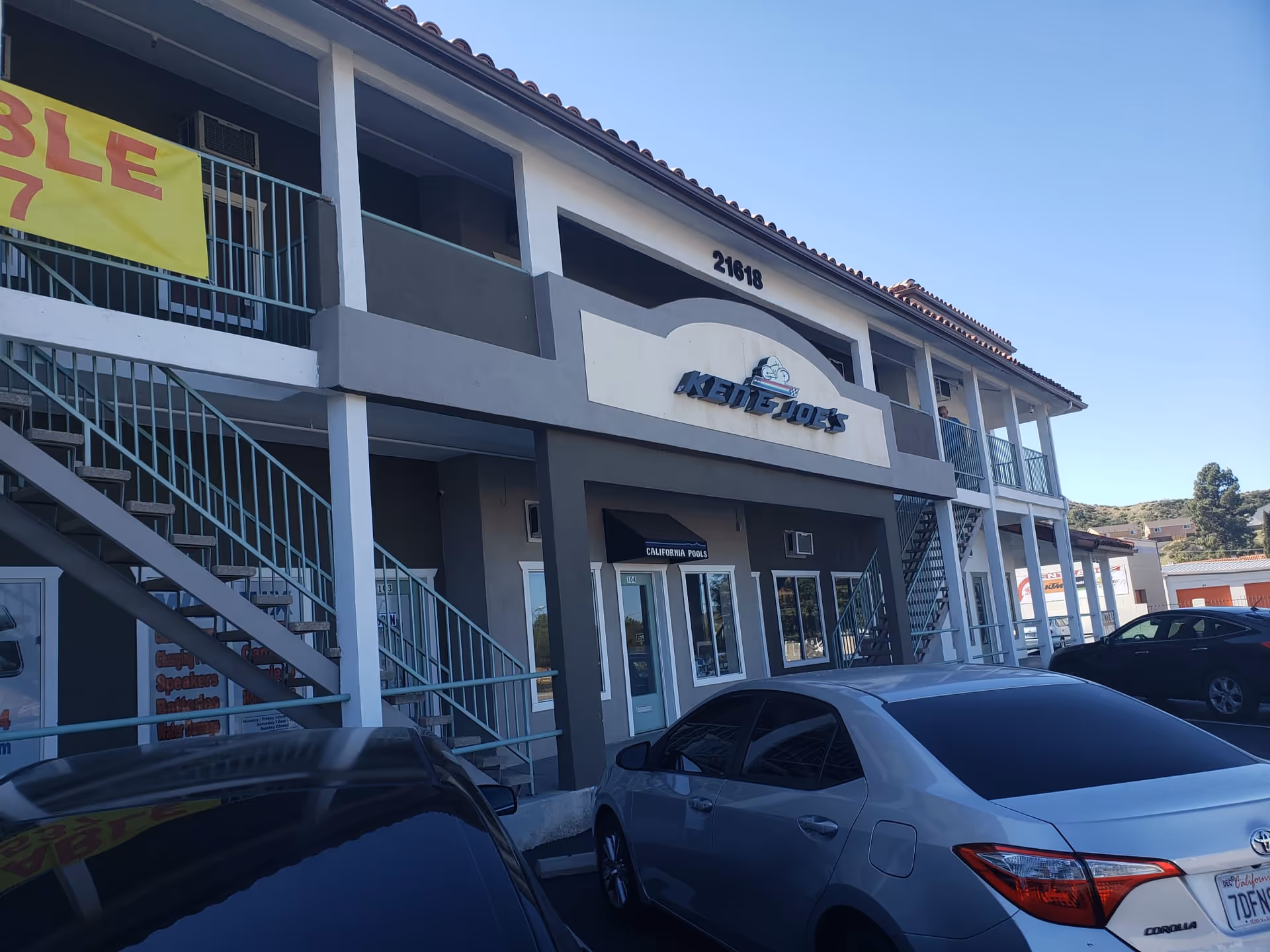 Two-story commercial building with external stairs, a parking lot, and storefront signage.