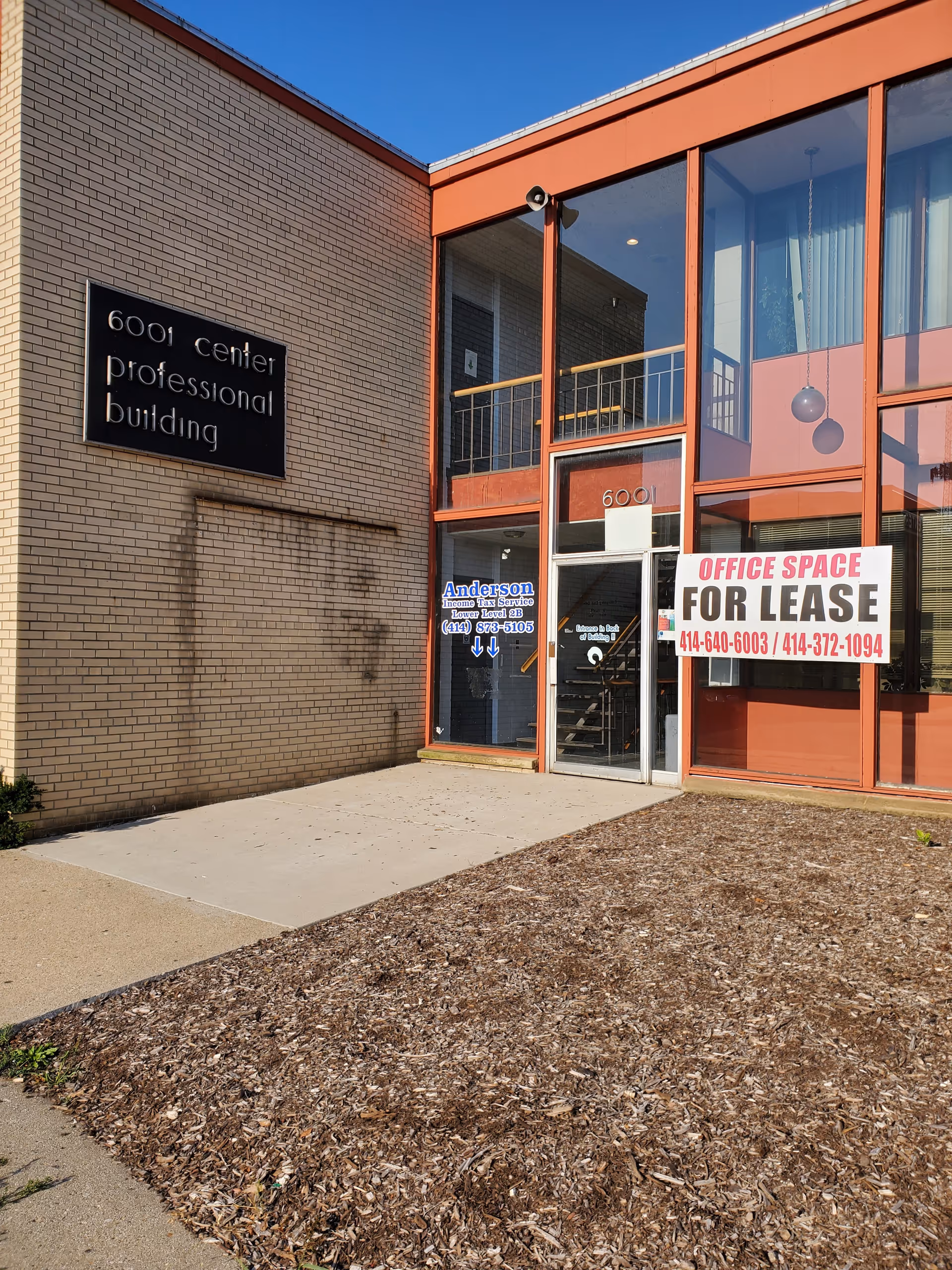 Exterior view of a brick professional building with glass entrance and lease sign.