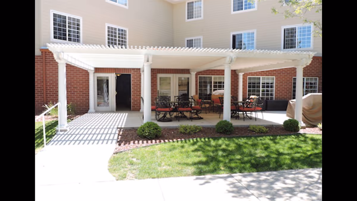 Back patio under a white pergola with tables and chairs outside a brick building.