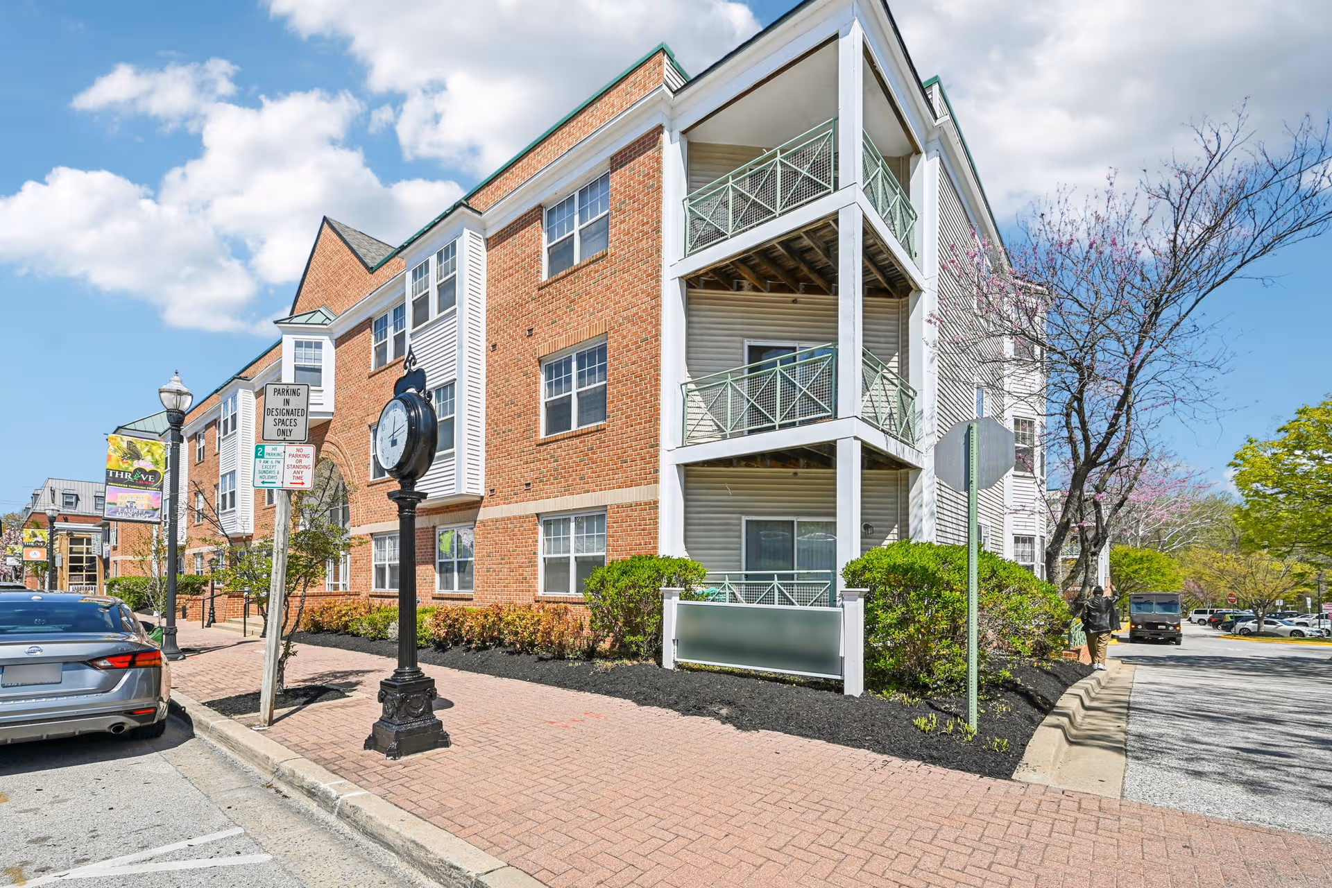 Brick, multi-story senior living building with balconies along a sunny street.