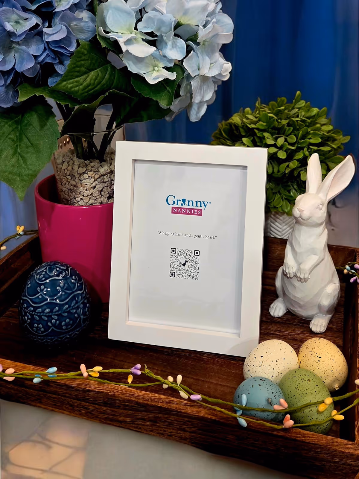 Framed Granny Nannies sign on a wooden tray with flowers, bunny statue, and decorative eggs.