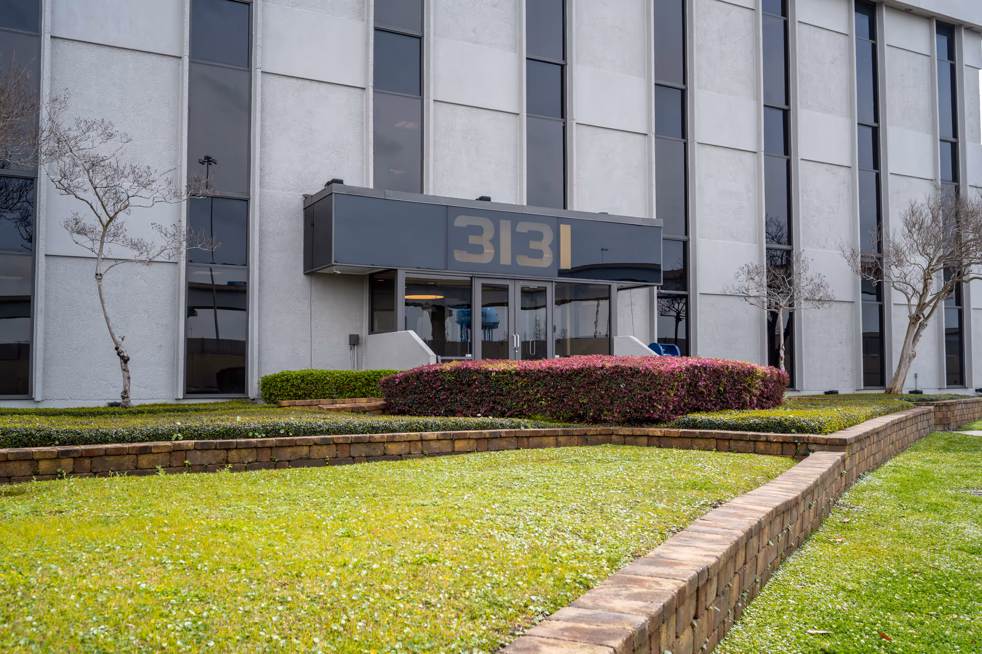 Exterior view of a modern building entrance with landscaped front yard.