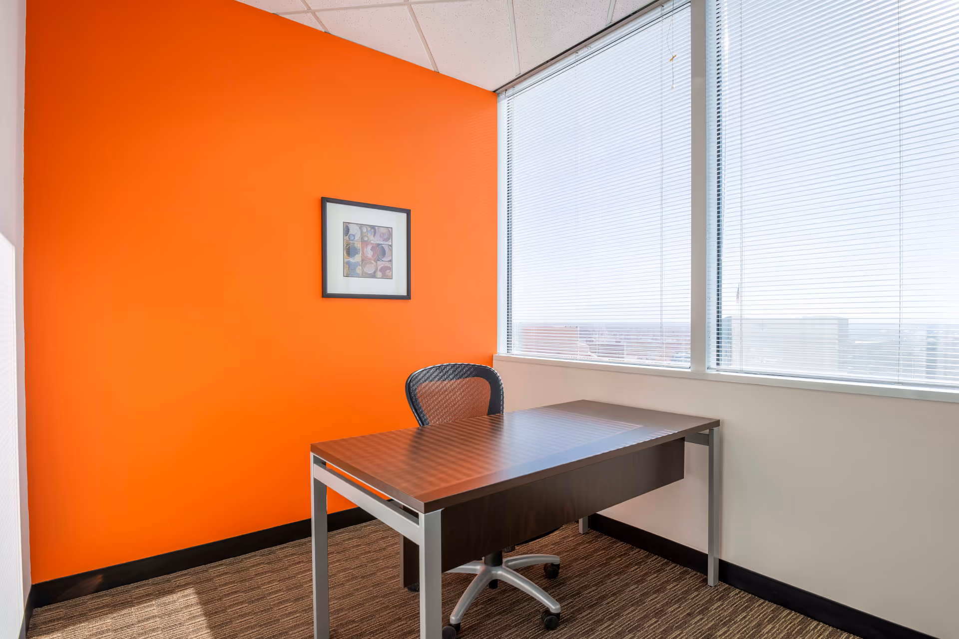Office workspace with an orange accent wall, desk, chair, and large windows.