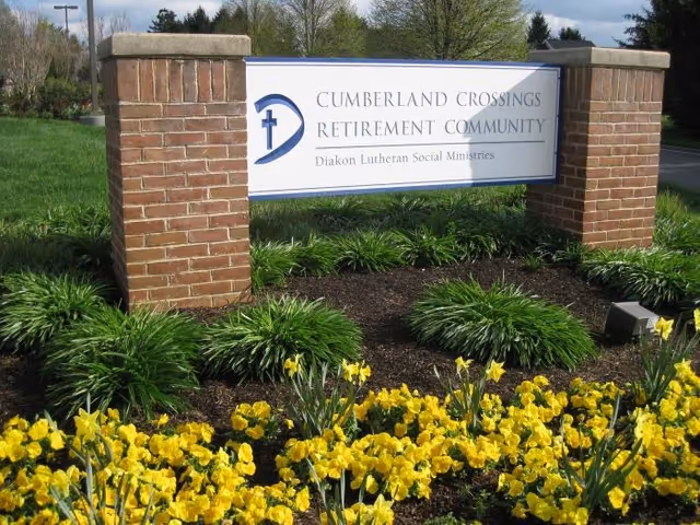 Brick sign for Cumberland Crossings Retirement Community with yellow flowers in the foreground.