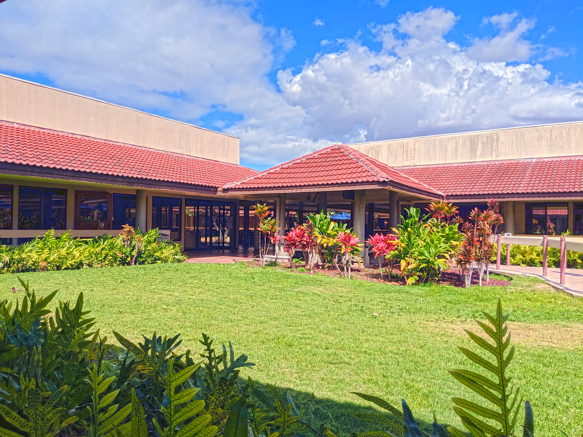 Sunlit exterior view of Hale Makua Health Services with red-tiled roof and tropical landscaping