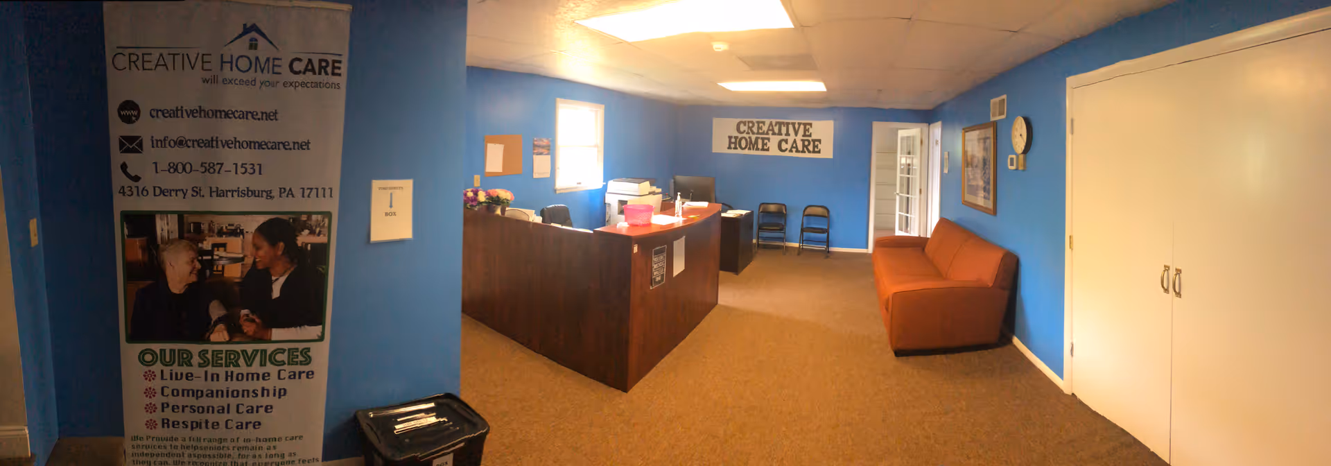 Reception area of a blue-walled senior care facility with a desk, chairs, and an orange sofa.