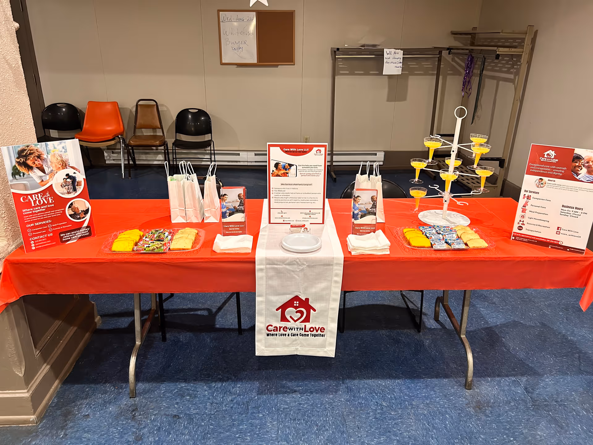 Promotional care booth with brochures and yellow beverage cups on a red-clothed table.