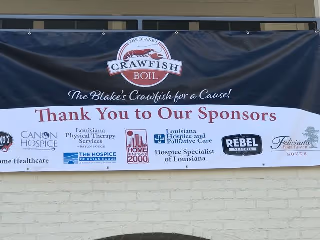 Exterior wall banner advertising sponsors for a Crawfish Boil event displayed on a beige brick wall.