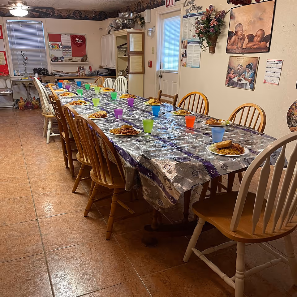 Long communal dining table with plates of food and colorful cups in a senior living facility
