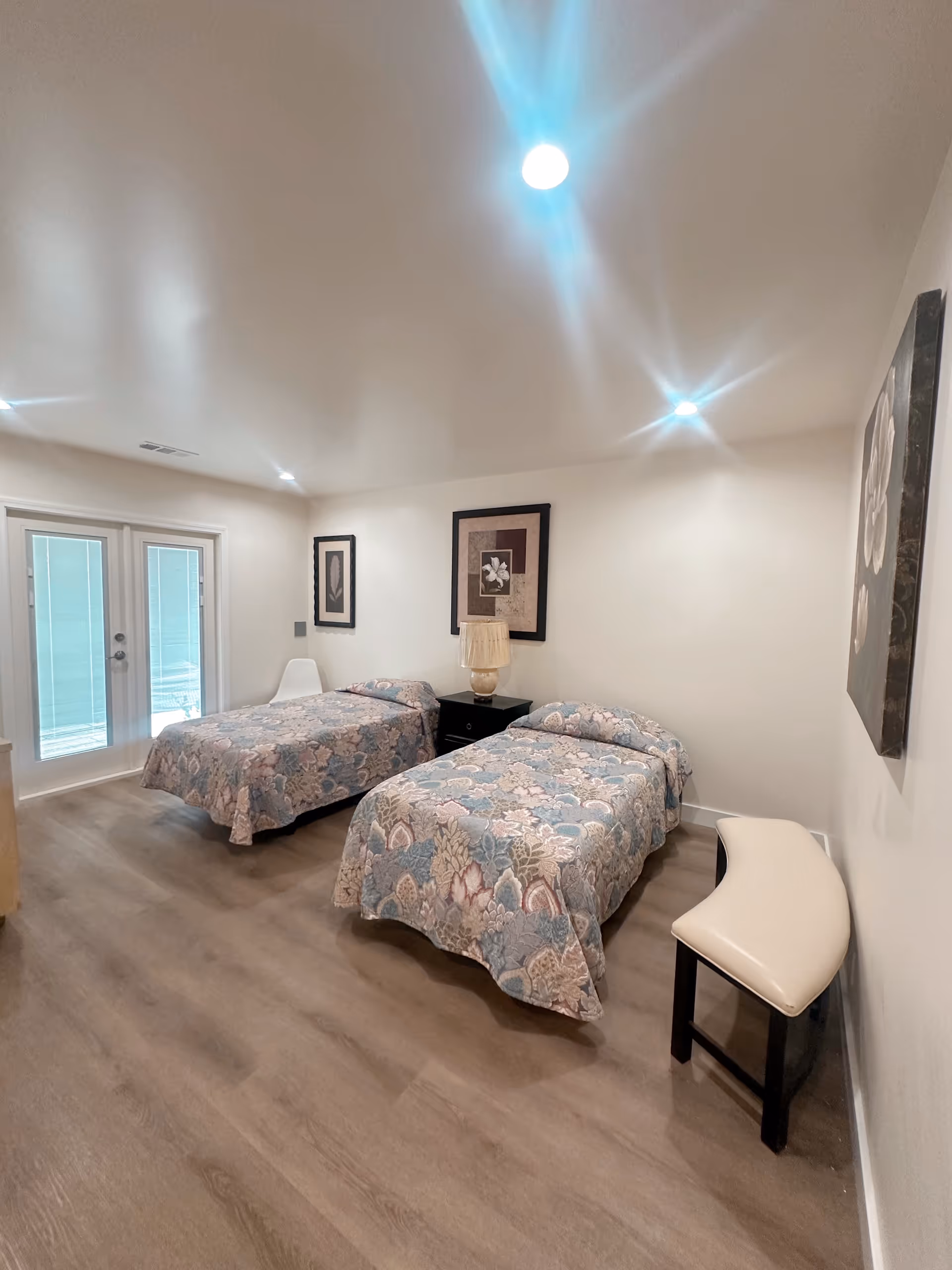 Two twin beds with floral bedspreads, nightstand, lamp, and framed wall art in a bedroom.