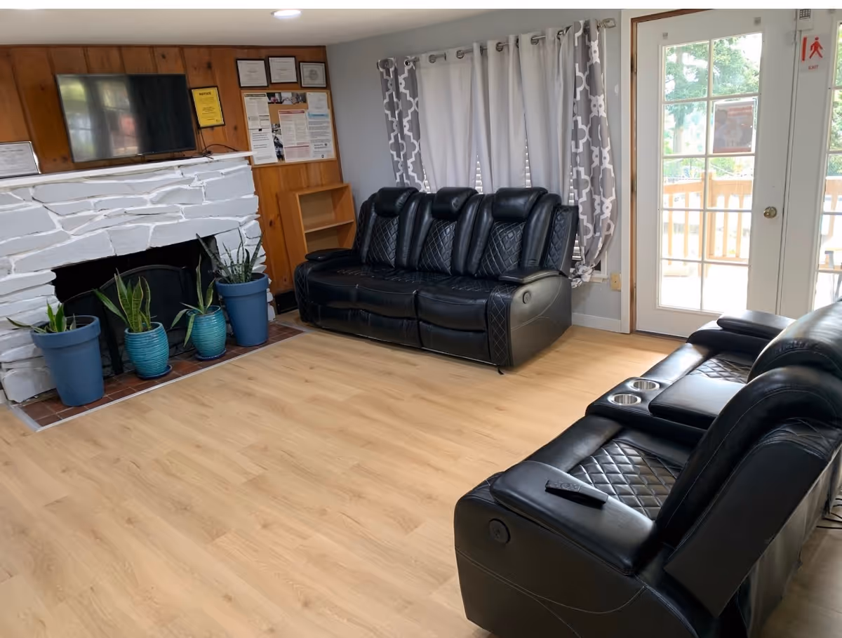 Cozy common living room with black leather recliners, fireplace, potted plants, and a glass door.