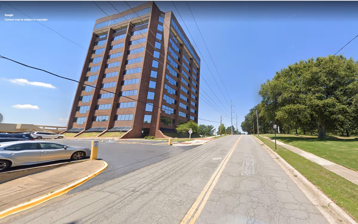 Exterior view of a tall brick senior living building on a street with cars and trees.