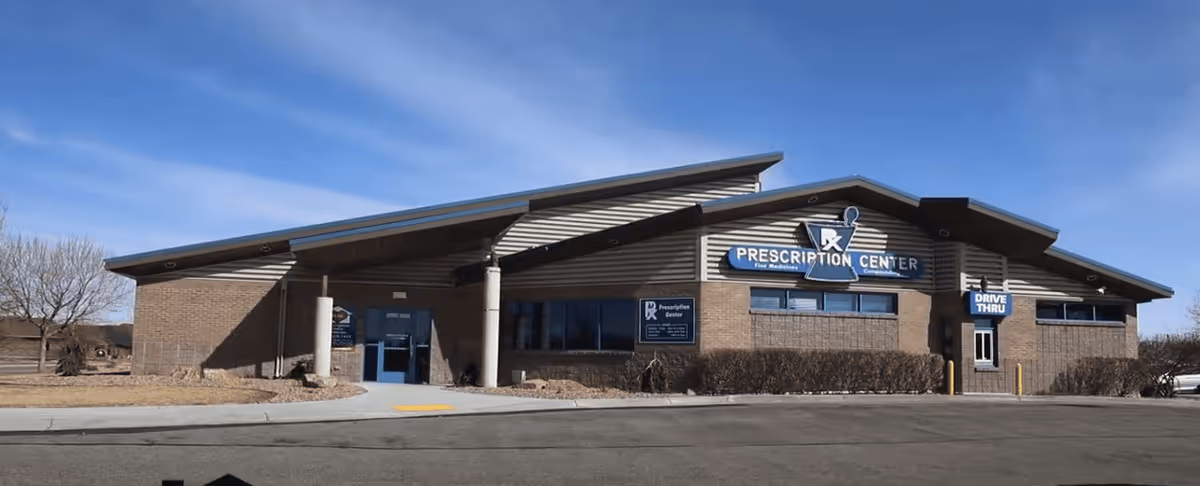 Brick facility exterior with a blue Prescription Center sign and drive-thru entrance.