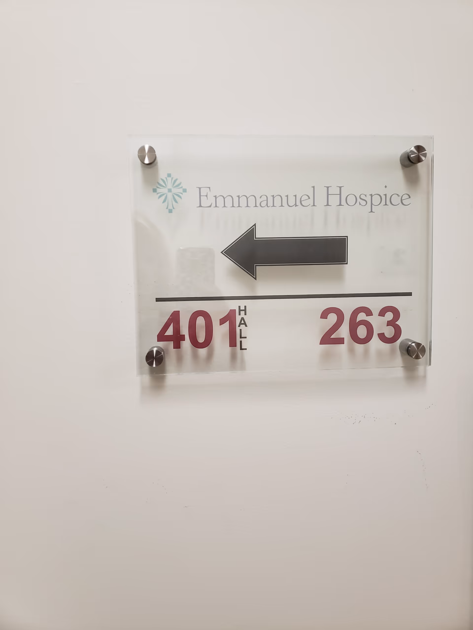 Clear acrylic wall sign reading Emmanuel Hospice with a left-pointing arrow