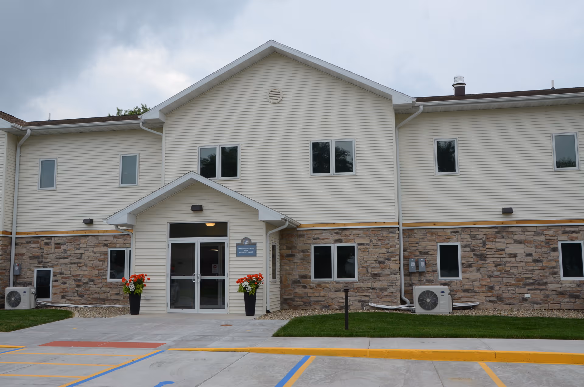 Facade of Hammond Center for Assisted Living with beige siding, stone lower wall, glass entrance.