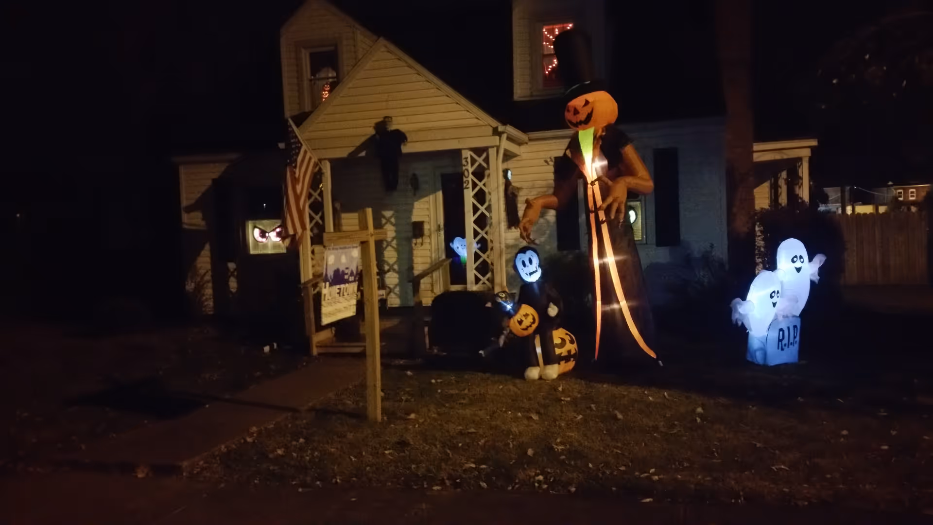 Night exterior of a house front with Halloween decorations, pumpkins and inflatable figures.