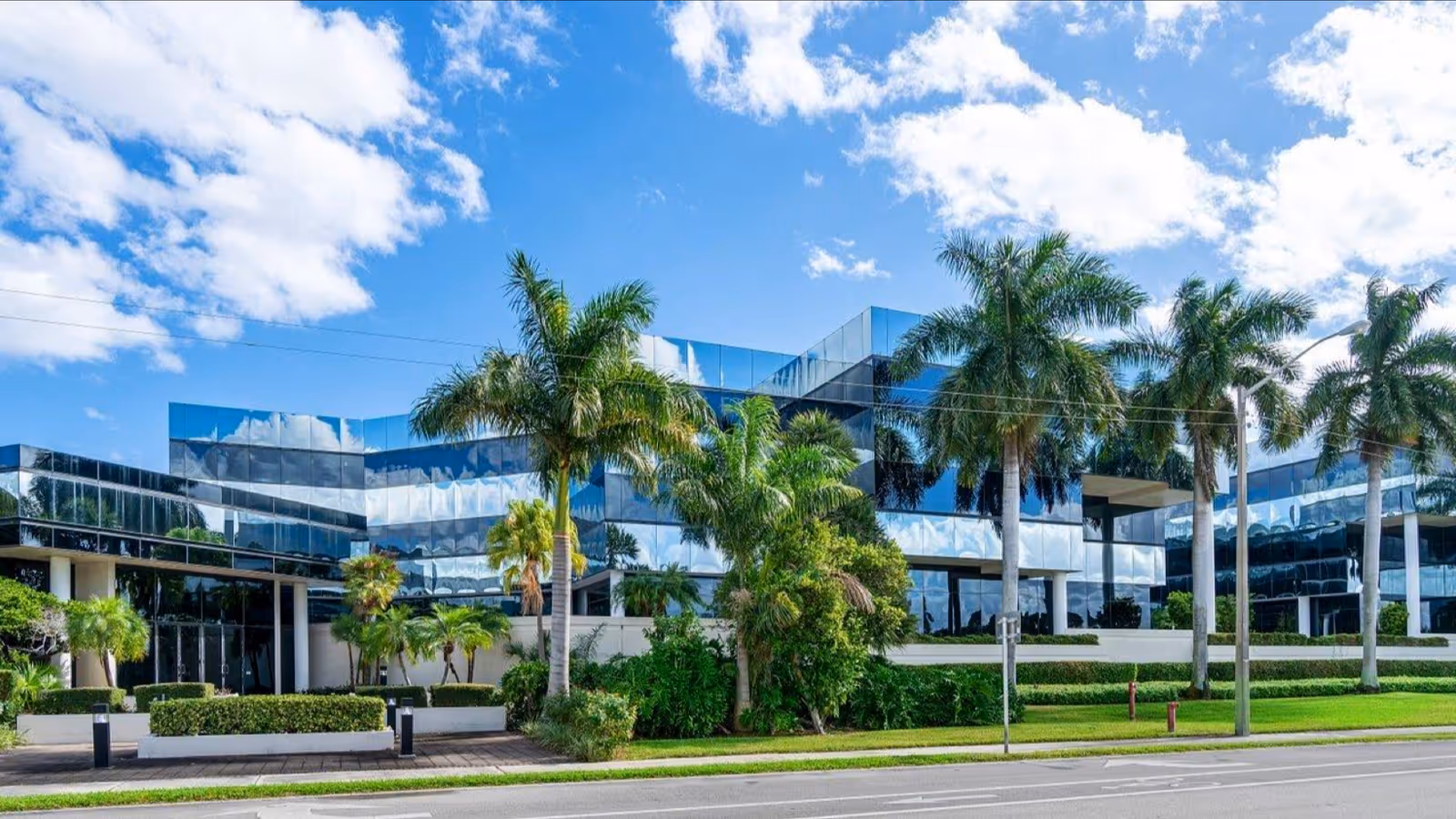 Modern glass-front senior living building with palm trees under a blue sky.