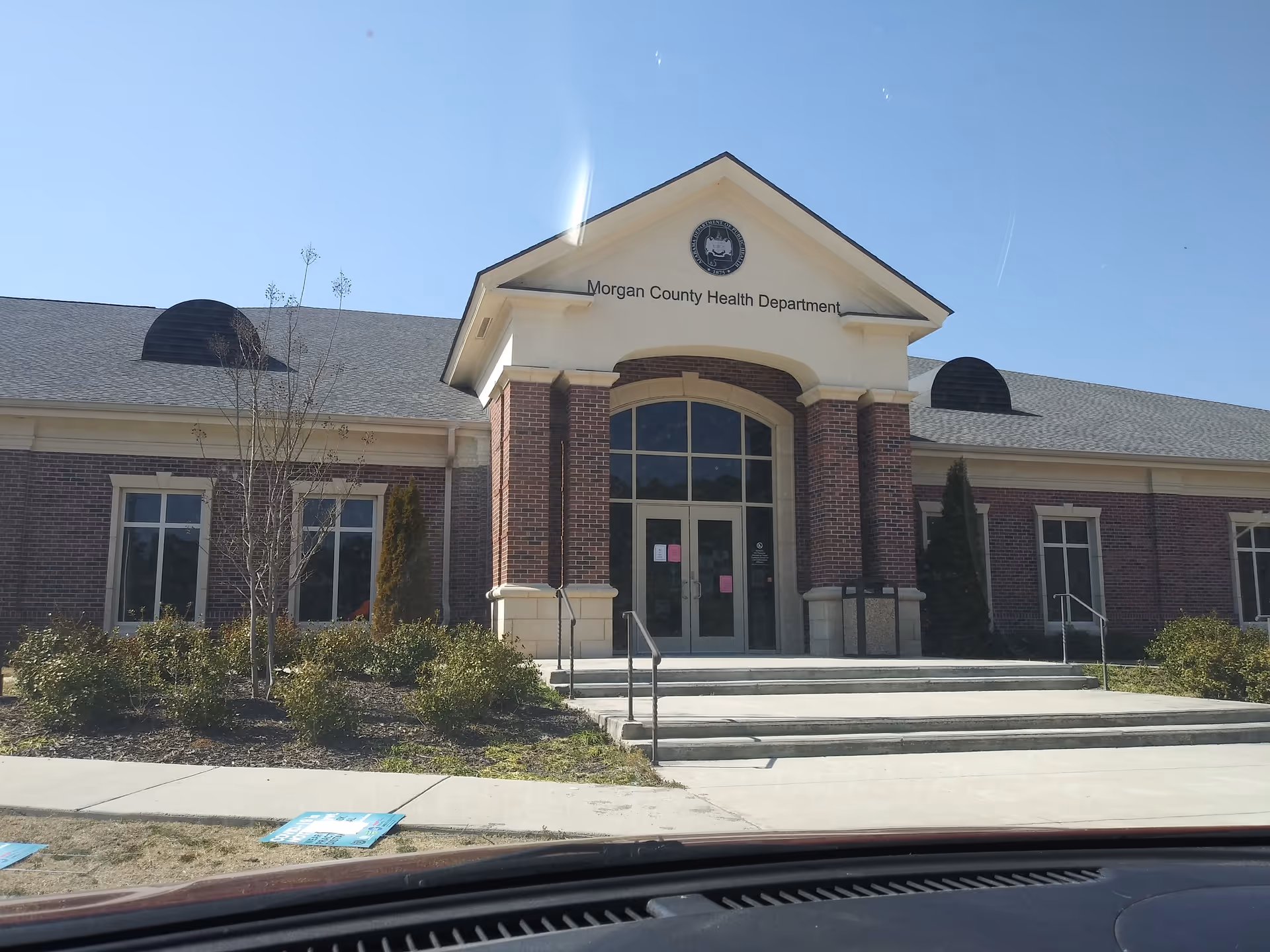 Brick government building with arched entrance labeled Morgan County Health Department against a clear blue sky.