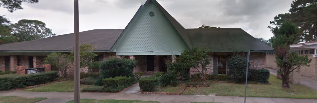 Single-story brick senior living facility with a peaked green entrance and well-kept landscaping.