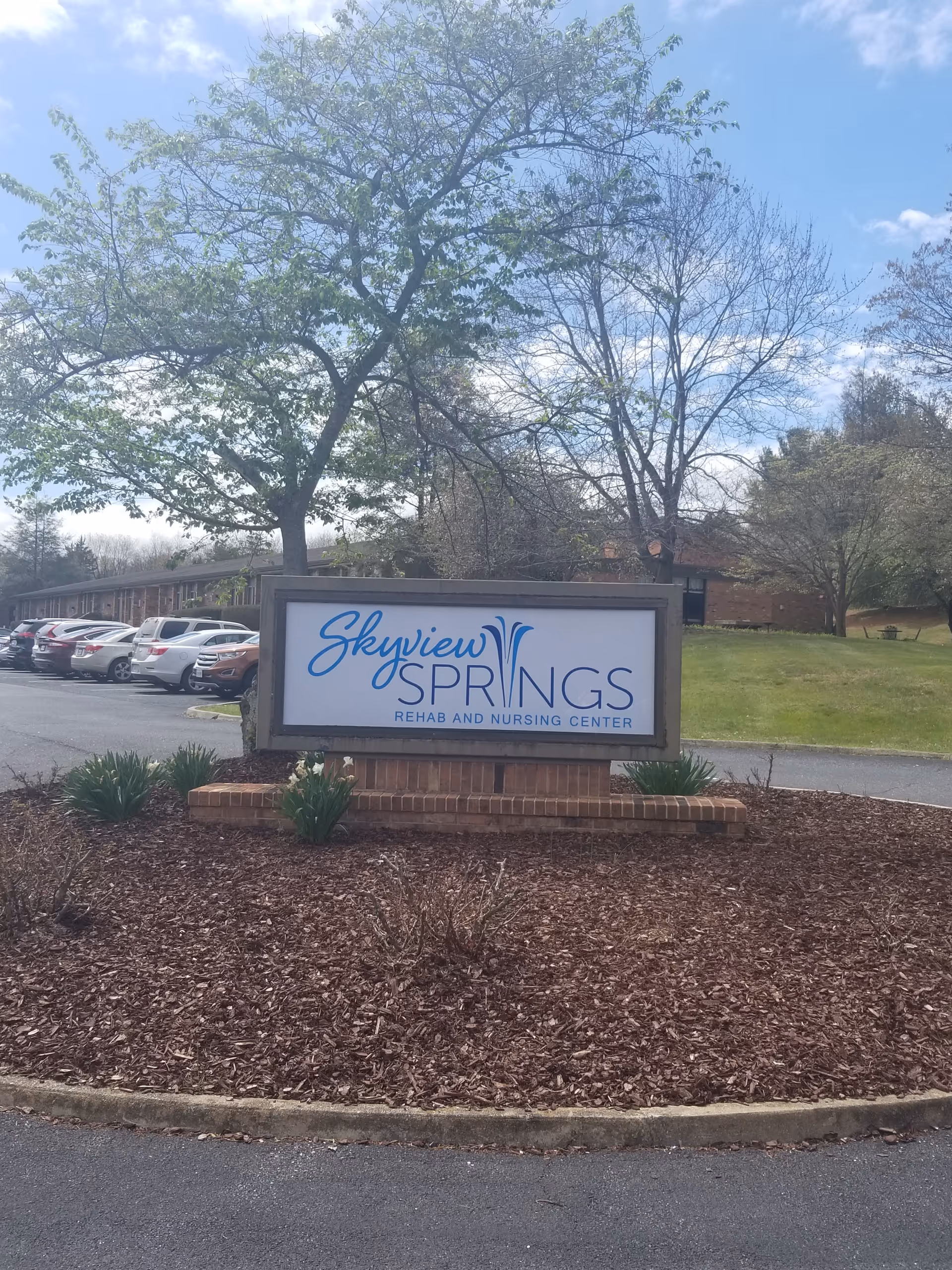 Outdoor view of Skyview Springs Rehab and Nursing Center sign with parked cars and trees.