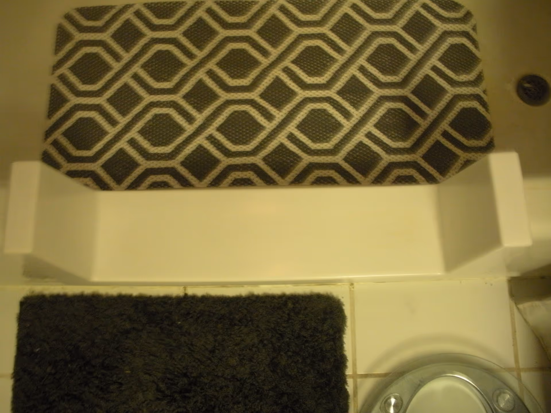 View of a bathroom floor with a patterned rug, step, and dark bath mat.