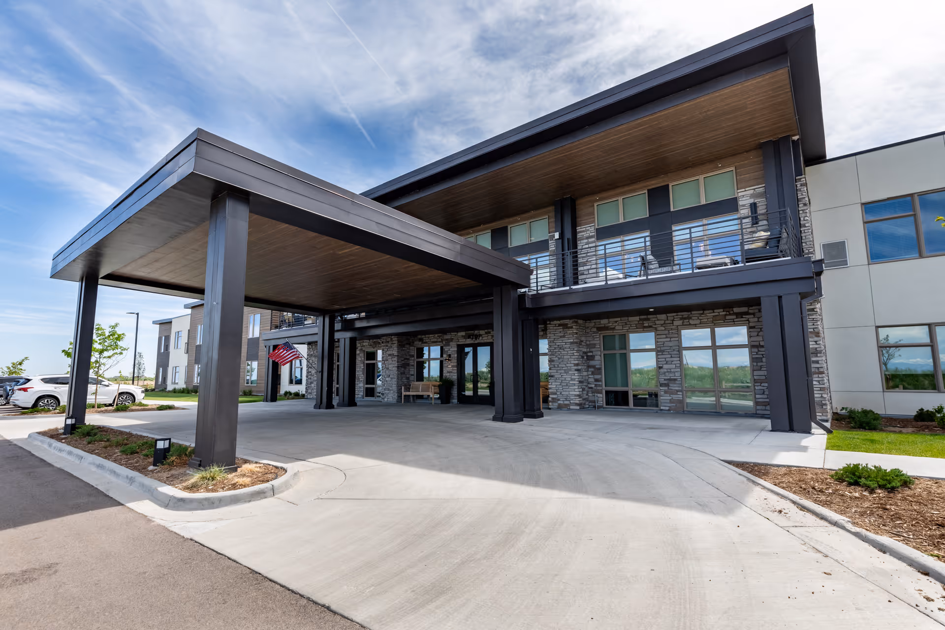 Front exterior view of a modern senior living facility named Terra Bluffs, featuring a covered entrance with large pillars, stone and wood accents, and multiple windows under a partly cloudy sky.