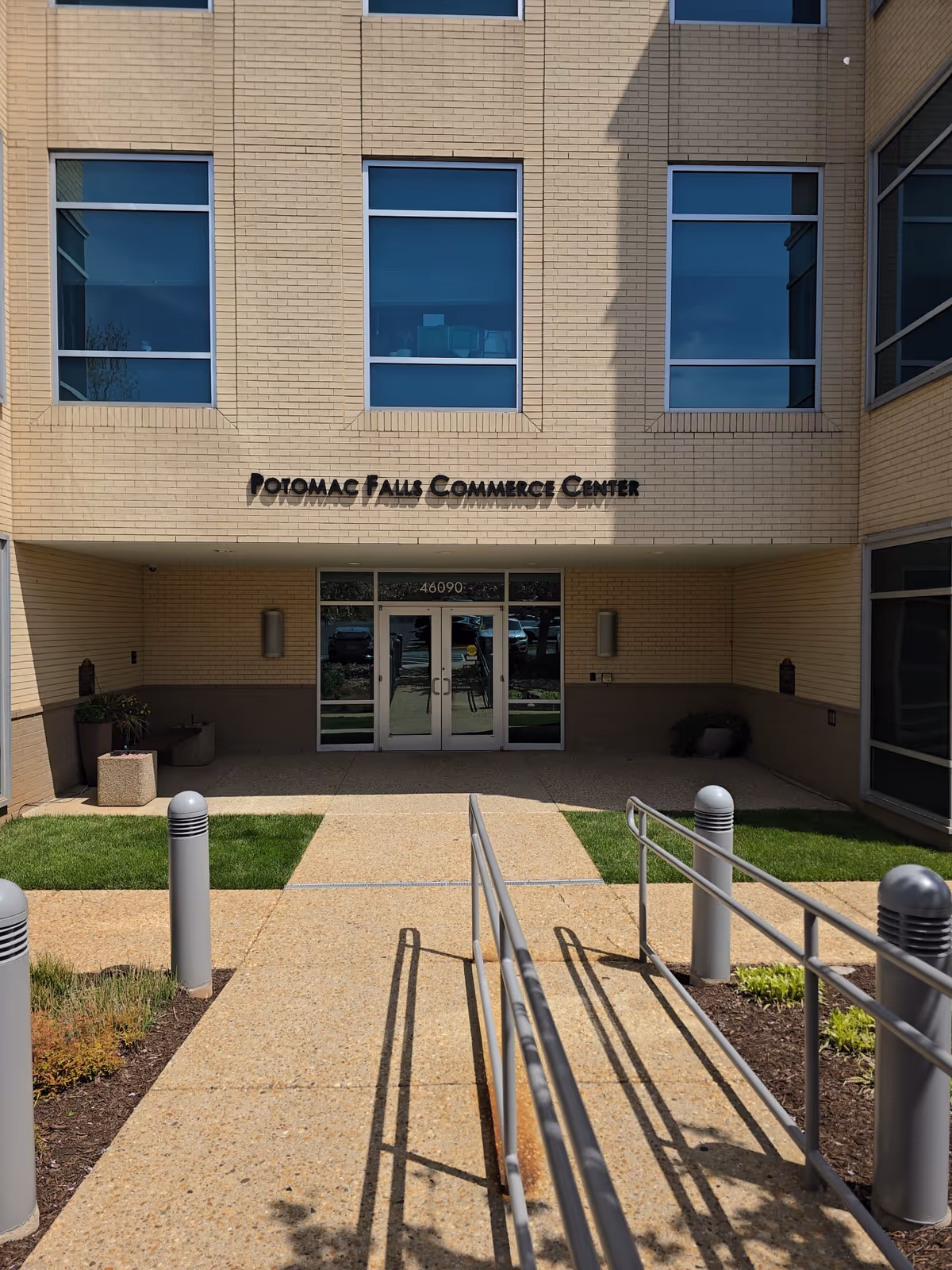 Exterior view of a brick building entrance with glass doors and ramp.