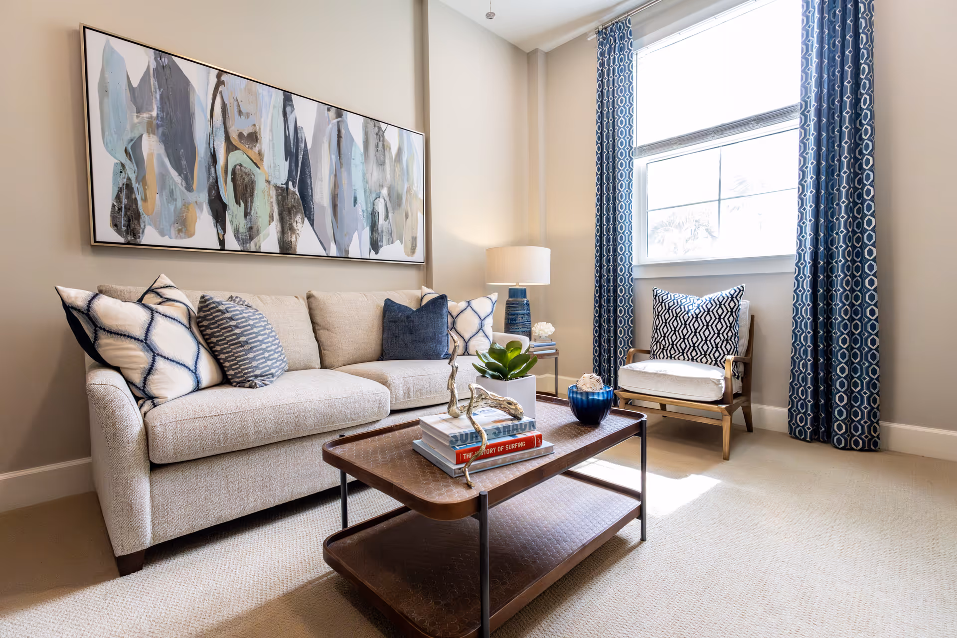 Bright living room with beige sofa, abstract art, coffee table, and blue curtains.