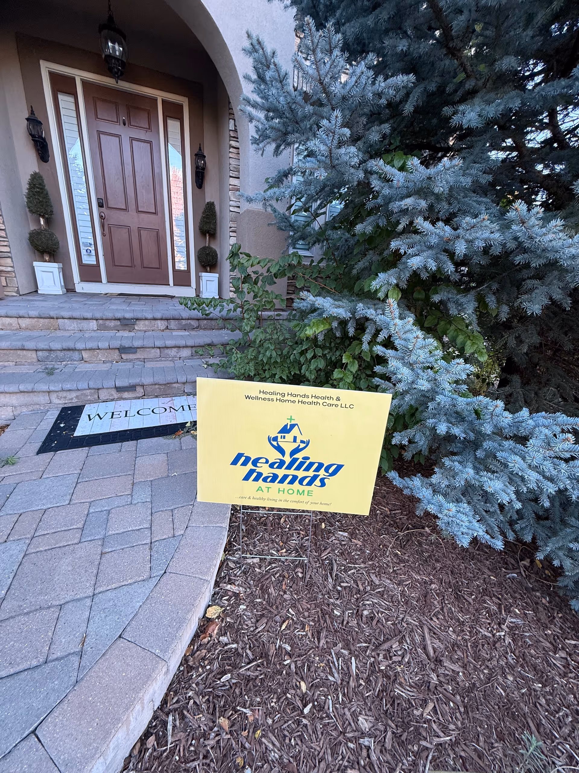 An exterior view of the Healing Hands entrance with a yellow sign and landscaped walkway.