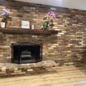 Brick fireplace with wooden mantle and potted plants in a cozy lounge.