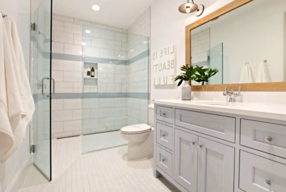 Bright modern bathroom with glass shower, tiled walls, toilet, and a blue-gray vanity.