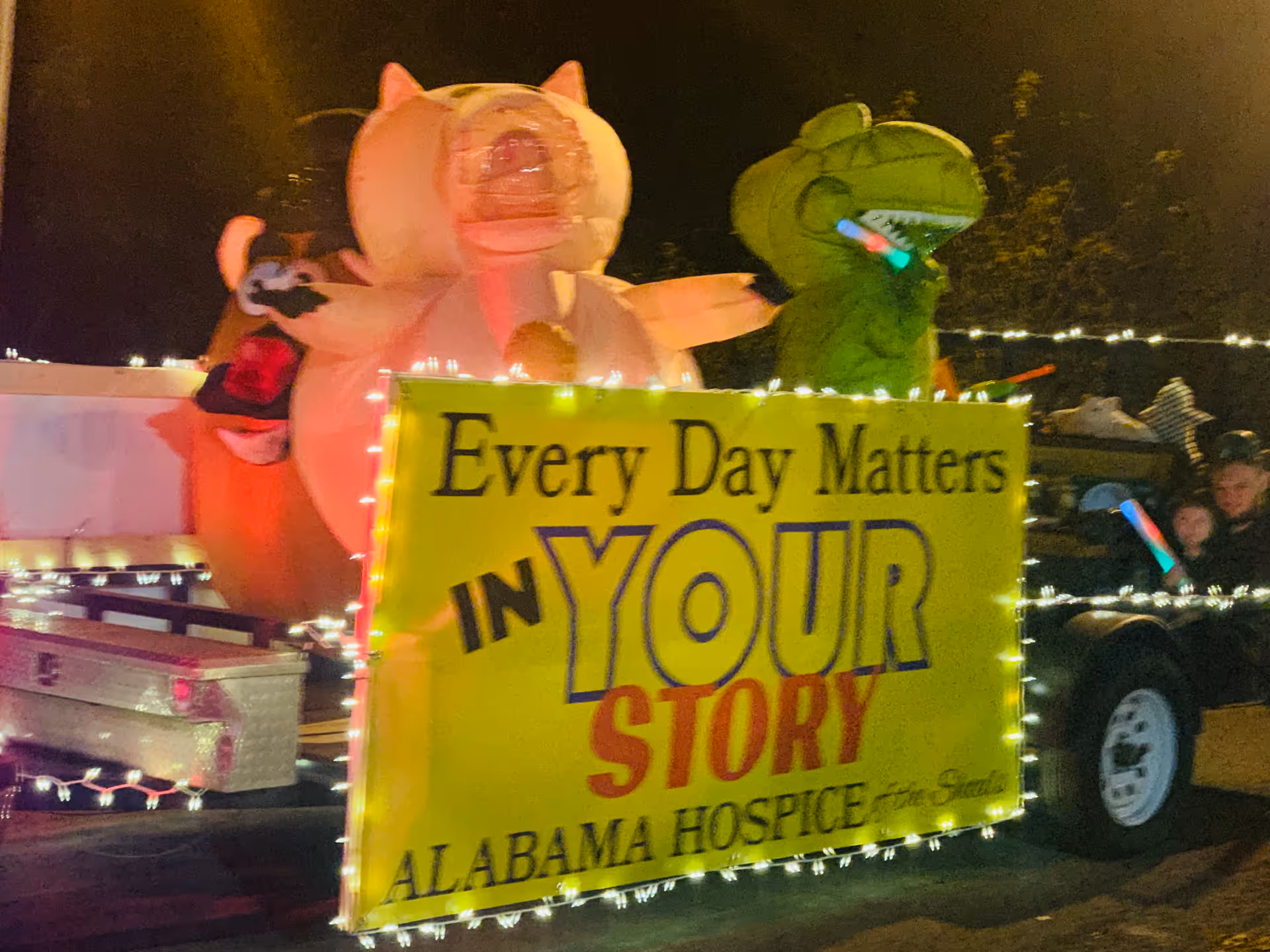 Night parade float featuring a bright yellow banner for Alabama Hospice of the Shoals.