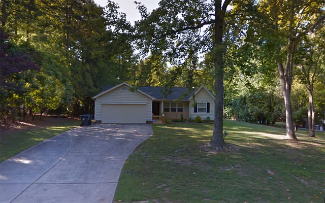 A single-story house with a curved driveway, front yard, and trees.