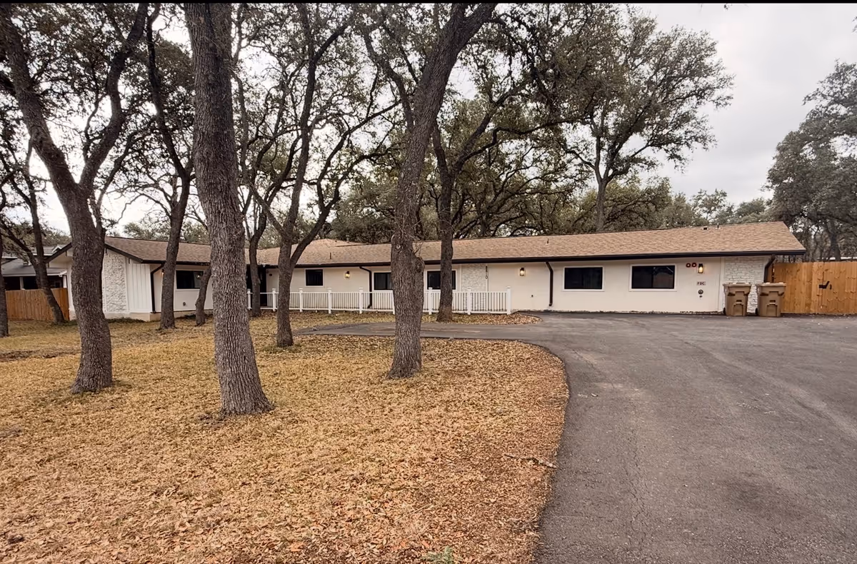Exterior view of a single-story assisted living facility with a curved driveway and trees.